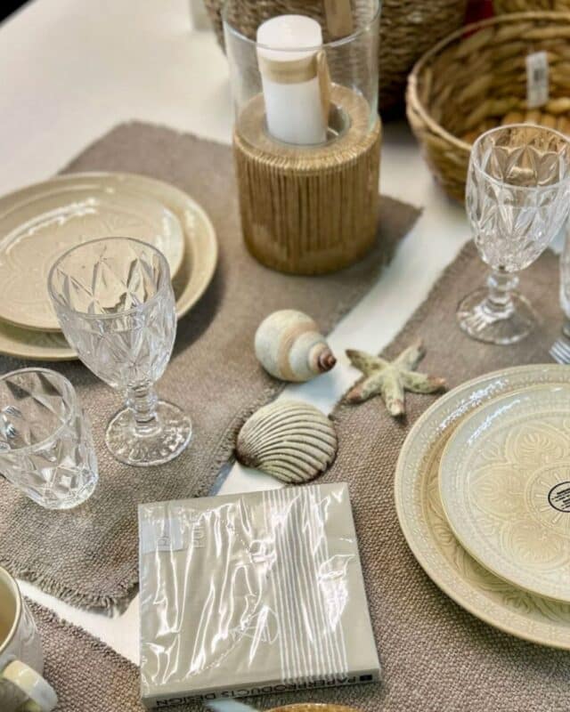 Mediterrane Dekoration einen Esstisch. Beigene Tischsets, mediterane Teller und ein Windlicht in der als mittiger Eyecatcher.